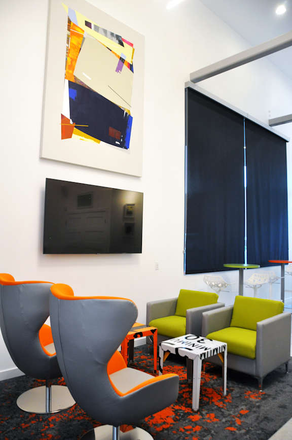 A modern living room with a grey and orange chair, a green couch, and a painting on the wall. at Liberty Square Apartments - Saltlake City, UT Apartments, Saltlake City