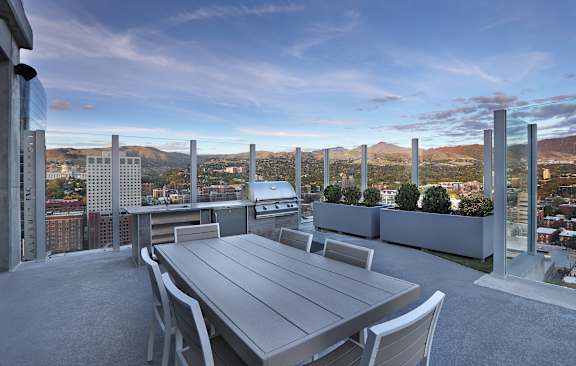 A table and chairs are set up on a rooftop terrace with a view of the city.