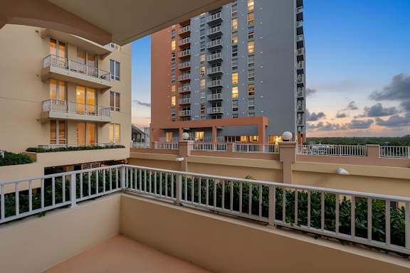 A balcony with a white railing overlooks a cityscape at dusk.