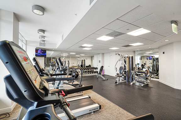 A treadmill is in the foreground of a well equipped gym.