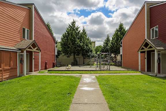 A playground with a slide and a green lawn in front of a red building.