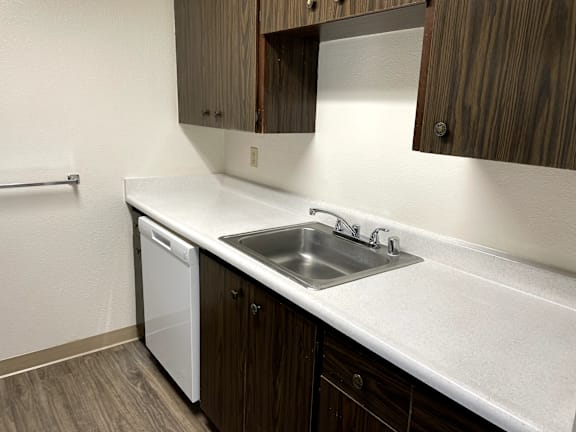 A white sink with a silver faucet is in a kitchen with brown cabinets.