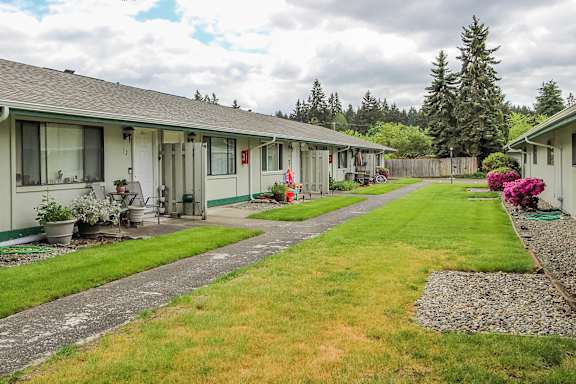 A row of houses with green lawns and trees in the background.