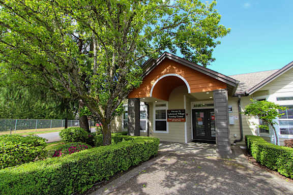 A building with a brown roof and a signboard is surrounded by green trees and bushes.