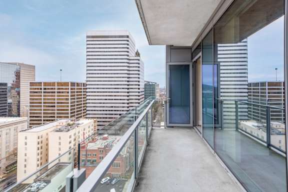 A balcony with a glass railing overlooks a cityscape.