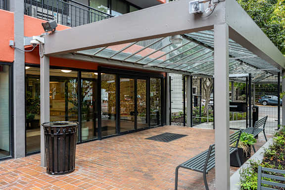 A glass door entrance to a building with a trash can and benches outside.