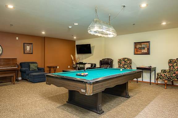 A pool table is in the middle of a room with chairs and a television.