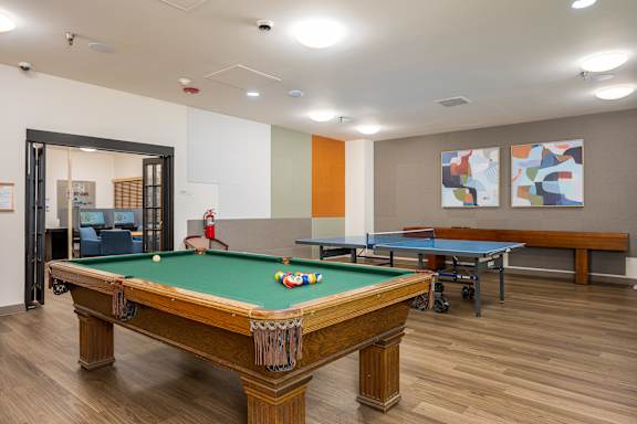 A pool table in a room with a ping pong table and two paintings on the wall.