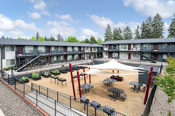 A courtyard with tables and chairs surrounded by a fence and apartment buildings.