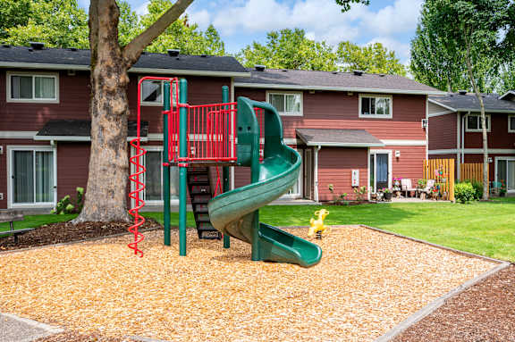 A red and green playground slide in front of a red house.