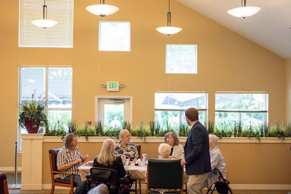 A group of people are sitting at tables in a room with a green exit sign on the wall.