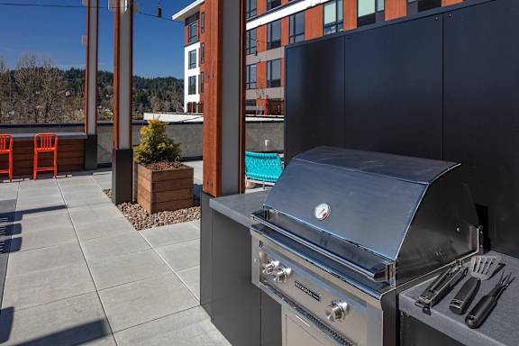A BBQ grill is on a patio with a pool in the background.