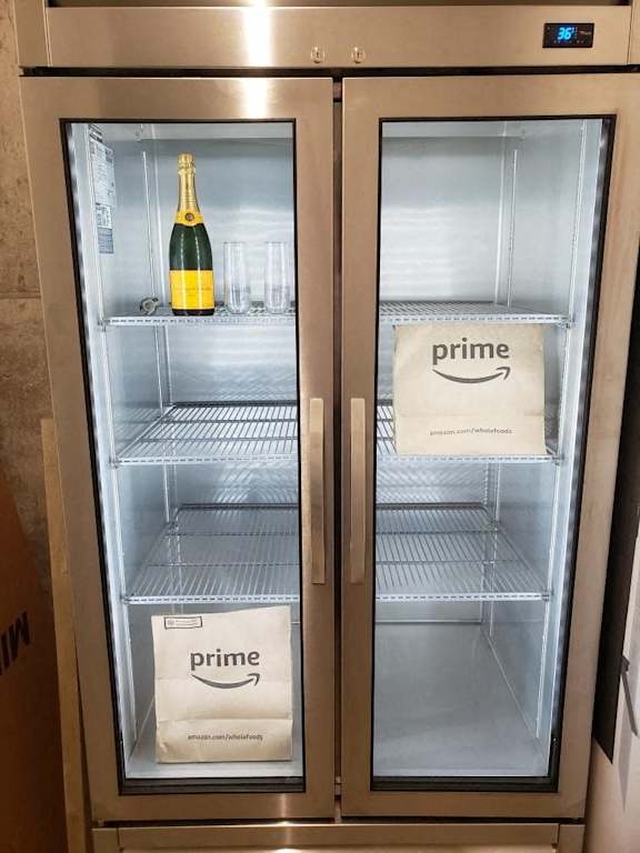 Two refrigerators, one with a bottle of champagne and one with a Prime bag.