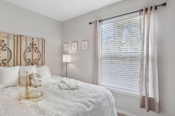 a large window with blinds and decorative window treatments and a bed in a Centerville Manor Apartment home