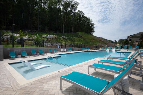 a swimming pool with blue chaise lounge chairs and a hill with trees in the background at Canopy Park Apartments, Alabama, 35124