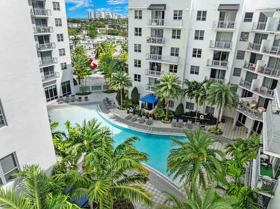 A pool surrounded by palm trees and a white building.