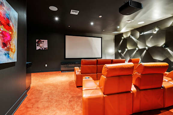 A room with orange seats and a large screen on the wall.