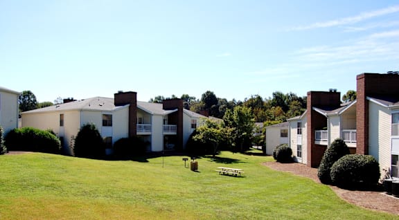 A grassy area in front of a building with a bench in the middle at Fox Hollow Apartment Homes, High Point