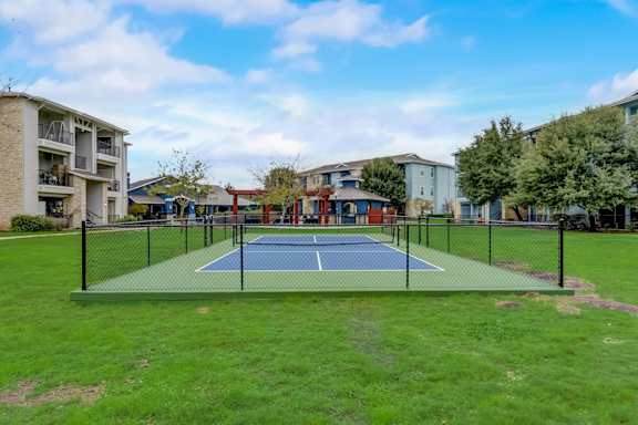 A tennis court is surrounded by apartment buildings.