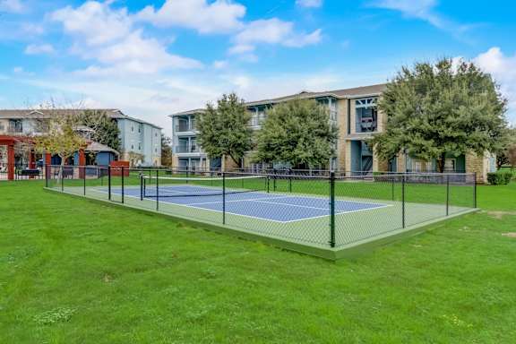 A tennis court is surrounded by a fence and apartment buildings.