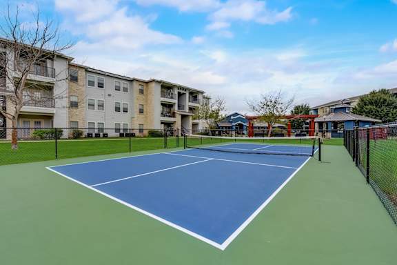 A tennis court is surrounded by apartment buildings.
