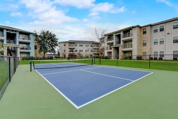 A tennis court is surrounded by apartment buildings.