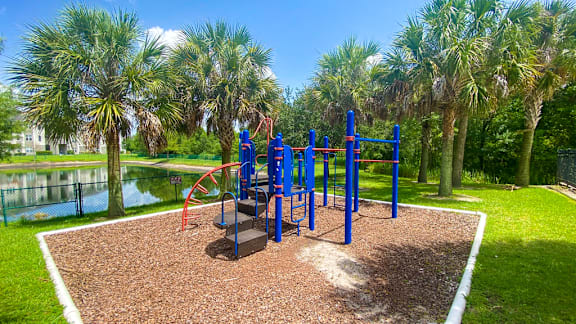 A playground with a red and blue swing set surrounded by palm trees.