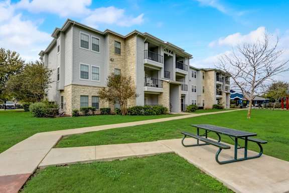 A large apartment complex with a green lawn and a picnic table in front.
