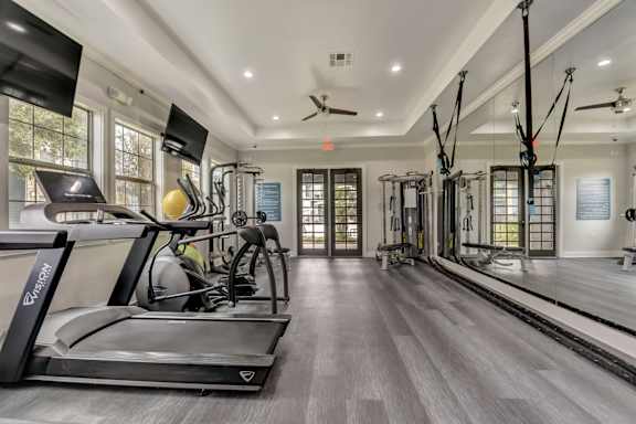 A spacious home gym with a treadmill, exercise bike, and suspension trainer.