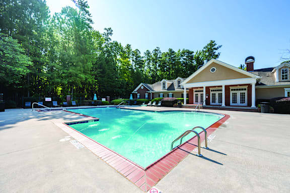 A large swimming pool surrounded by a red border and a house in the background.