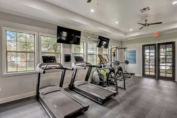 A spacious gym with treadmills, elliptical machines, and a fan.