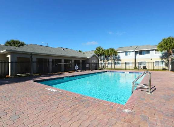 A swimming pool surrounded by a brick patio and a building in the background.