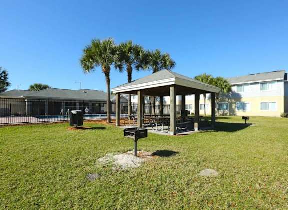 A gazebo sits in the middle of a grassy area with a building in the background.