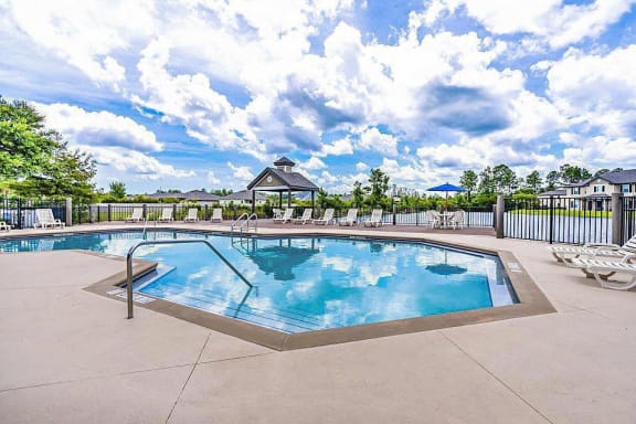 Irregular-shaped swimming pool and sundeck with tables, chairs, and loungers. The pool deck is situated on top of the lake.