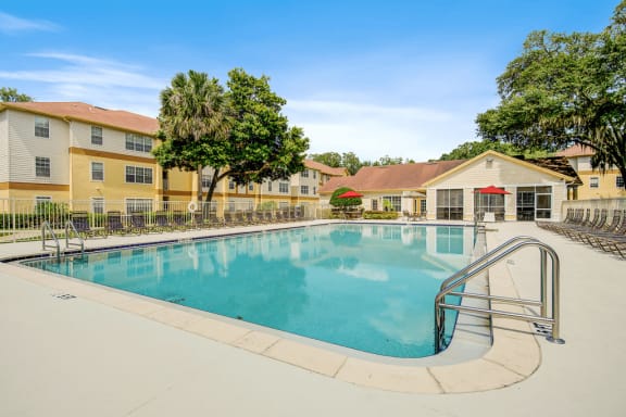 Swimming pool and pool deck featuring lounge chairs, red umbrellas, native landscape and the clubhouse in background