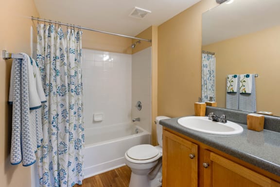 Bathroom with tile floors, toilet, shower tub combo with tile back splash, towel bar, brown wood cabinets