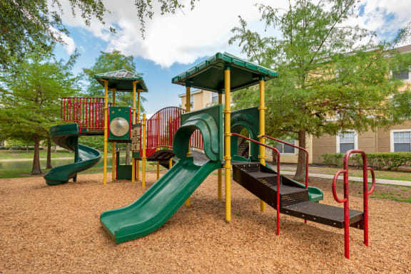 Playground jungle gym and playground slides in a bed of mulch with trees in the background