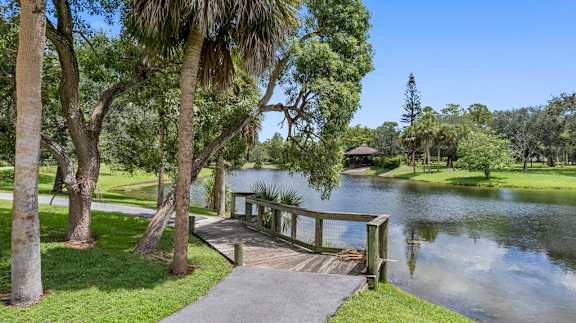 A wooden walkway leads to a gazebo over a calm lake surrounded by lush greenery.