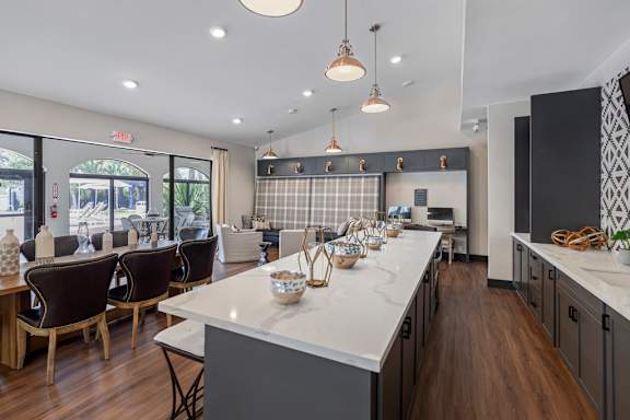 A kitchen with a long white island and dark chairs.
