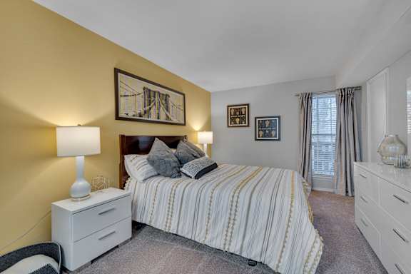 A bedroom with a bed, nightstand, and a painting on the wall.