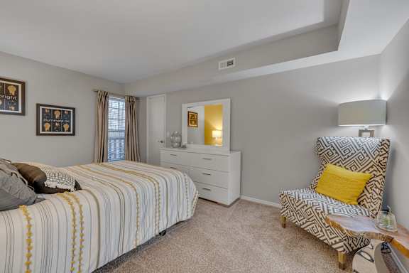 A bedroom with a bed, chair, and nightstand.