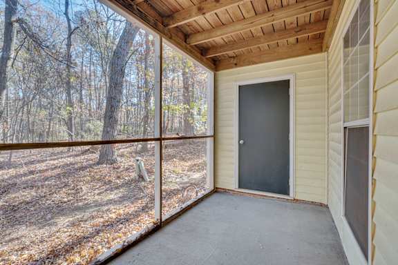 A screened porch with a sliding door leading to a wooded area.