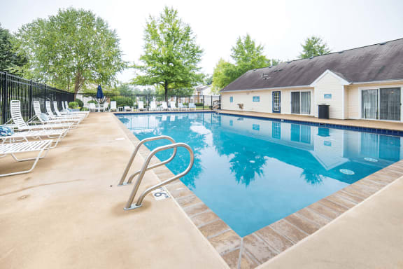 Swimming pool and sun deck with lounge chairs, pergola, and tables with umbrellas near treeline