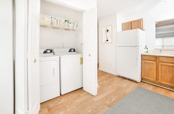 Virtually staged kitchen with grey rug, wood floor and white appliances. Laundry closet attached to kitchen.
