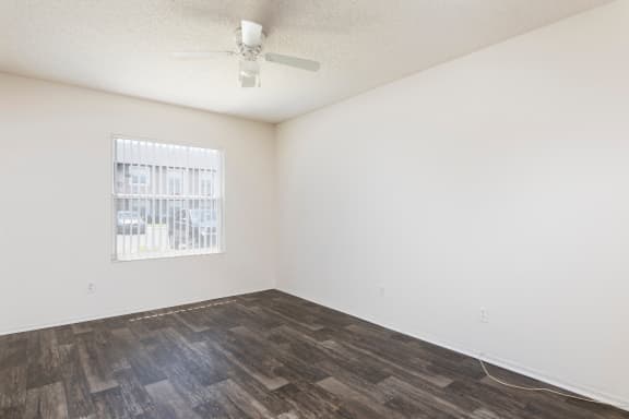 Bedroom with hardwood style flooring with white walls, a window and ceiling fan.