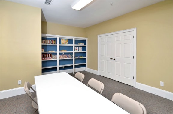 After school room with a book shelf on the back wall. Beige walls with double doors on the right side.