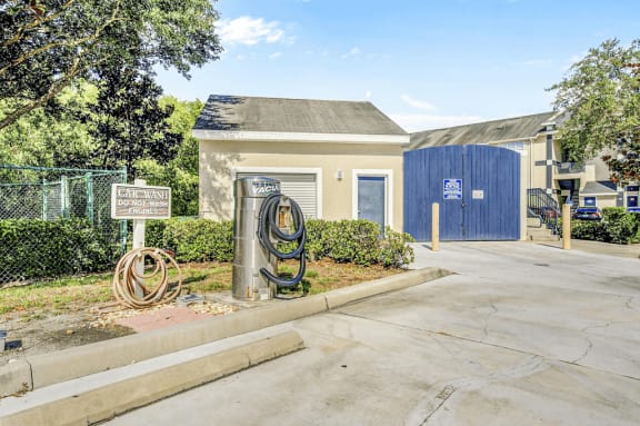 Car wash area with sprayer and vacuum in parking spot with surrounding native landscaping and utility room in background