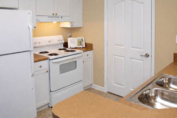 A white kitchen with a fridge, stove, and sink.