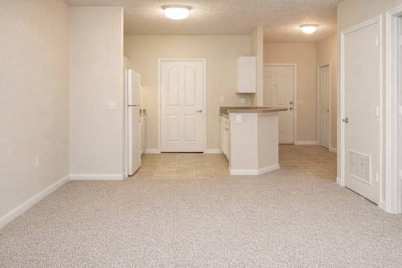 a carpeted living room with a view into the tiled kitchen