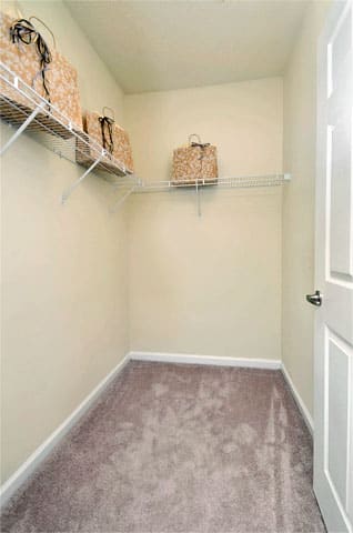 Apartment closet with tan carpet and beige walls. Wire shelving on two walls.